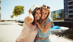 Two women smiling and holding each other on sunny day near the river