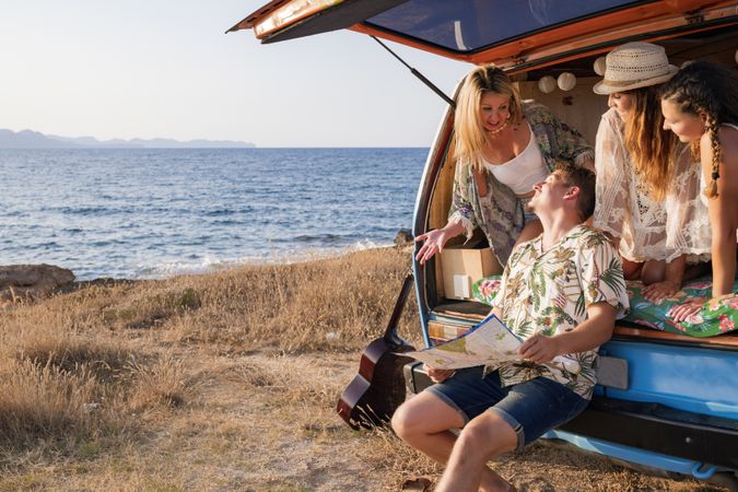 Puzzled man exploring map with help of long haired women in trunk of car