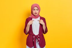 Incredulous woman in red headscarf pointing at herself questioningly