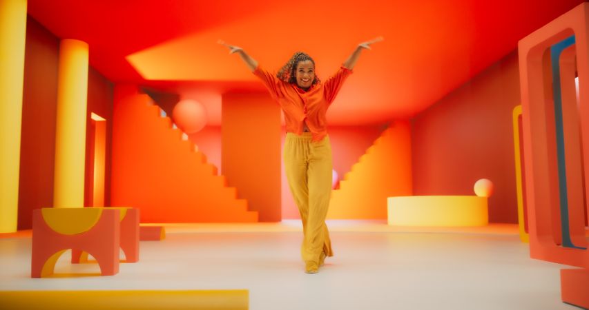 Black Woman in Bright Outfit Dancing Energetically in Geometric Abstract Orange, Yellow Environment.