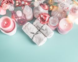 Spa and beauty cosmetic on blue desktop background with towels, candle and pink flowers. Top view