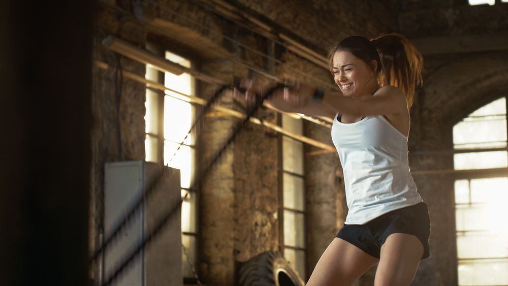 Athletic Female in a Gym Exercises with Battle Ropes During Her Cross Fitness Workout