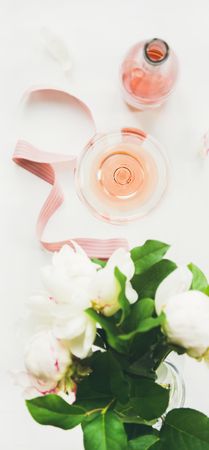 Glass of pink rose wine, and bottle with flowers and ribbon, vertical composition