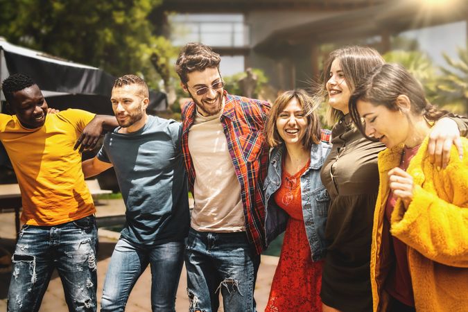 Multiethnic group of friends walking on street with arms on shoulders