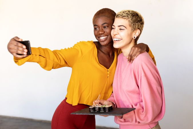 Smiling female couple taking selfie together over sushi lunch