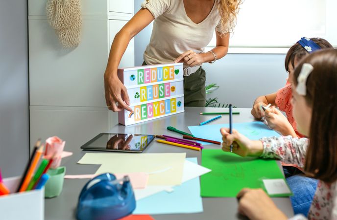 Teacher explaining to students a ecologic process using lightbox with text reduce, reuse, recycle