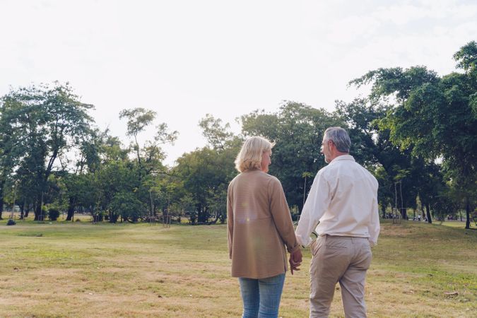 Rear shot of man and woman holding hands and walking in park