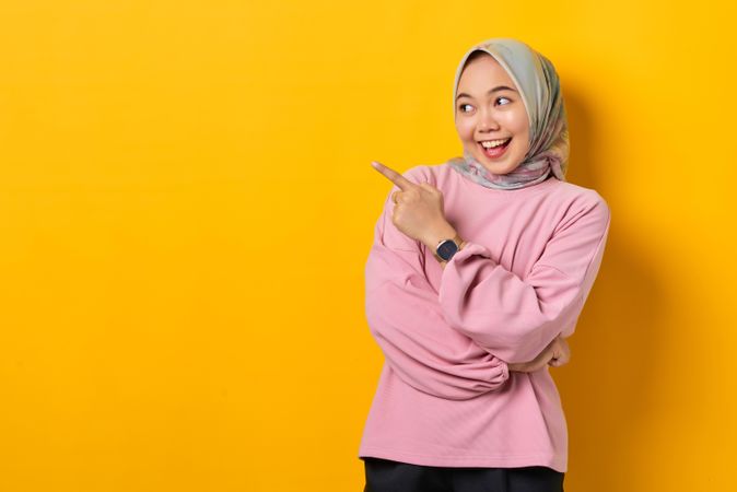 Excited Muslim woman in headscarf pointing to space beside her