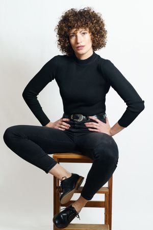 Stylish woman in dark outfit sitting on wooden bench with hands on hips