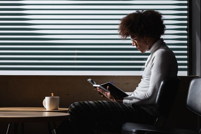 Focused young Black guy taking notes while chilling in cafe with cup of coffee