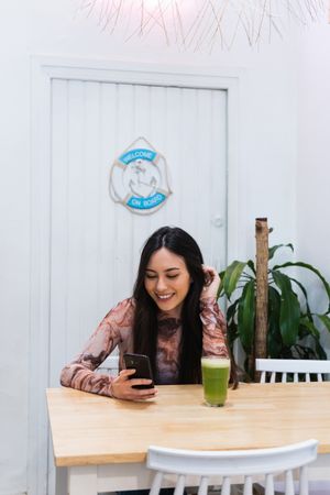 Smiling woman using smartphone at table in bar