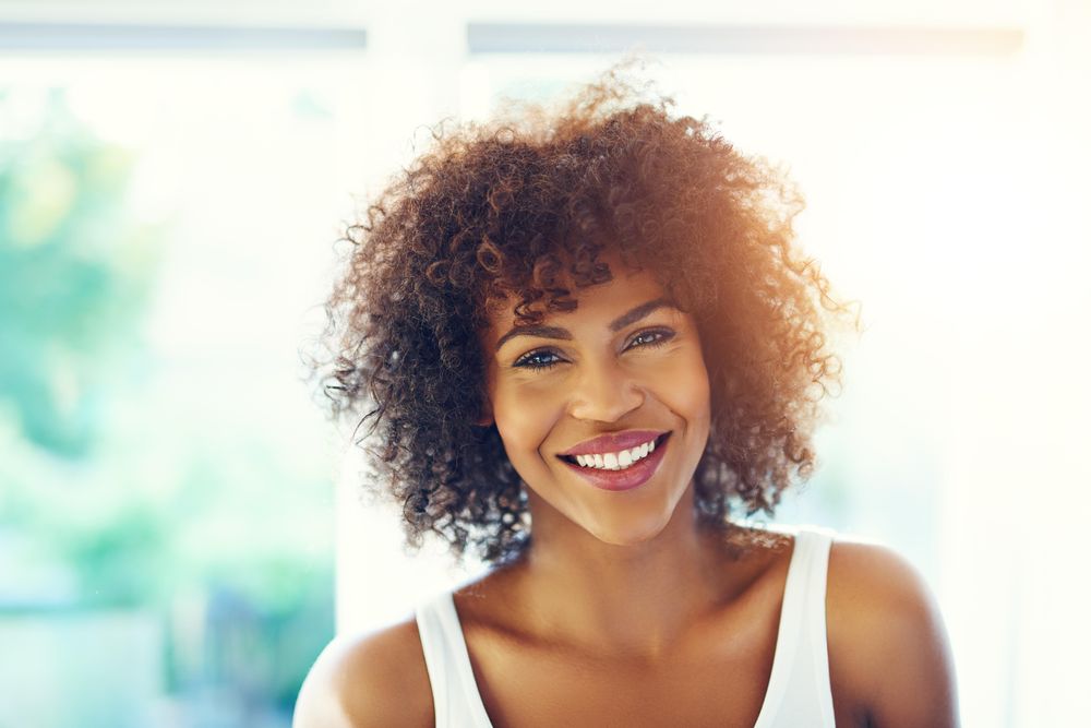 Confident smiling female with curly hair on leafy background