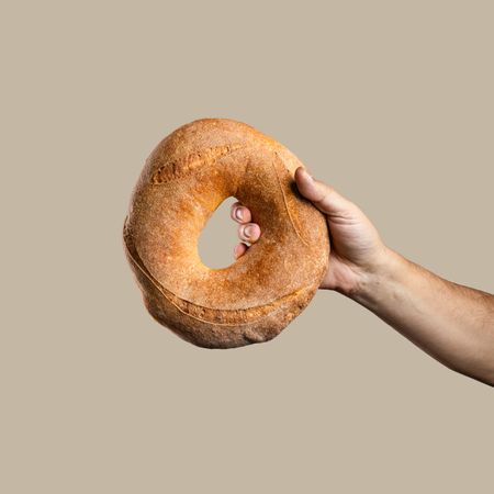 Hand holding a traditional round loaf of bread on a beige background.