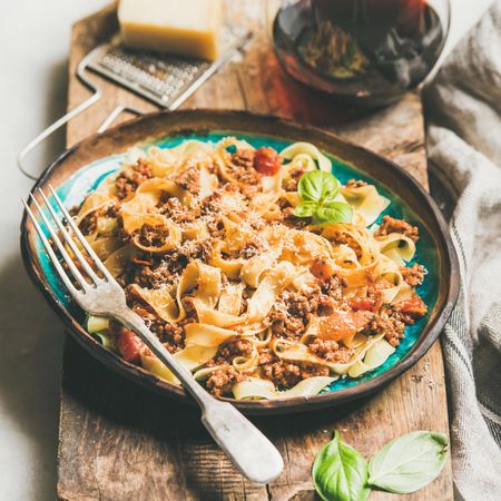 Pasta dinner with minced meat, cheese and red wine on wooden board, square crop