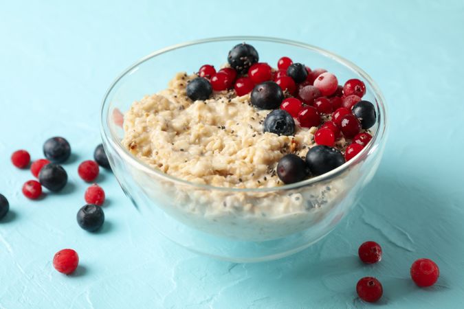 Bowl with oatmeal porridge and fruits on blue background