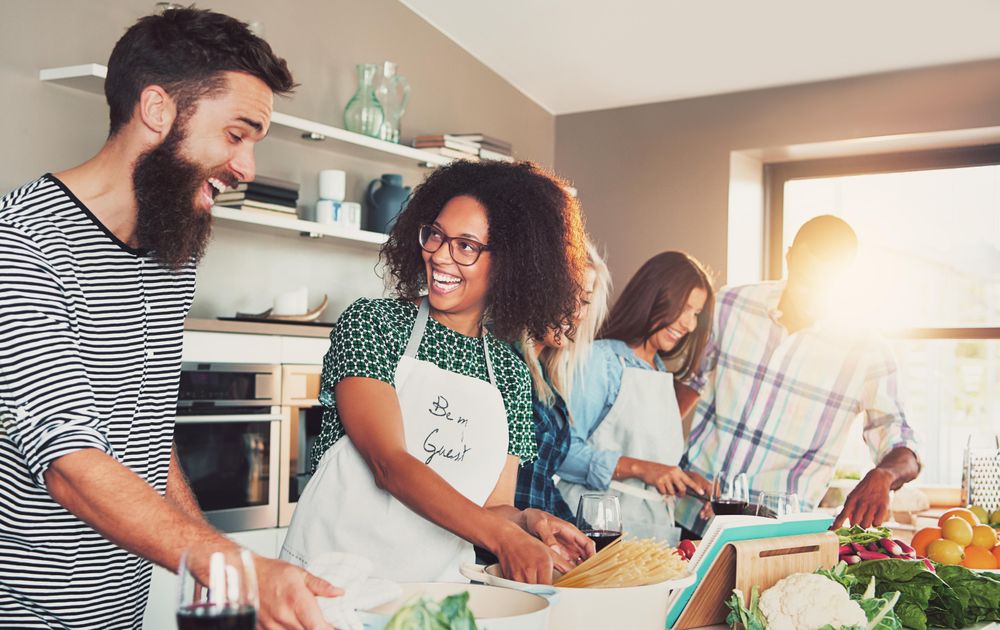Multi-ethnic friends joking together while cooking pasta