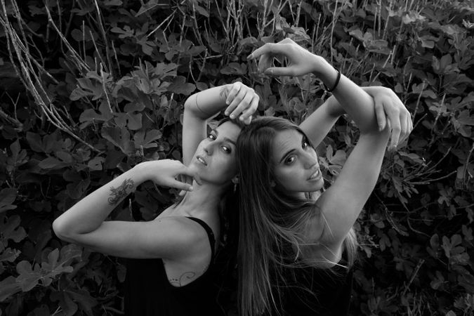 Young women posing near green bush