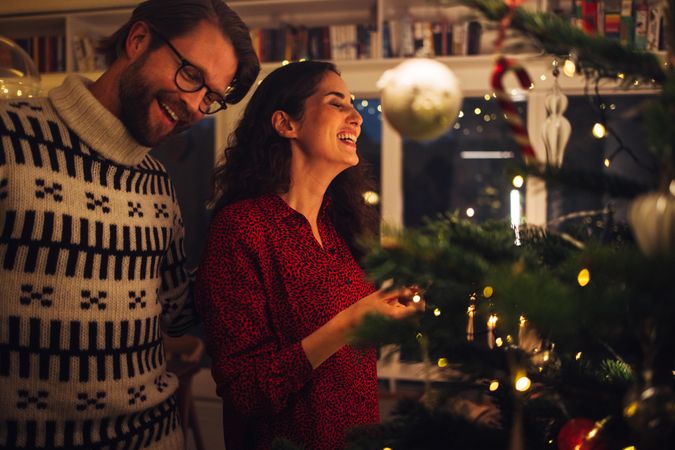 Man and woman smiling while decorating Christmas tree at home
