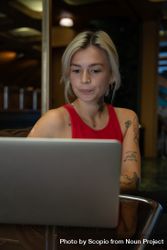 Young woman in red tank top typing on computer keyboard in a coffee shop 48E6Xb
