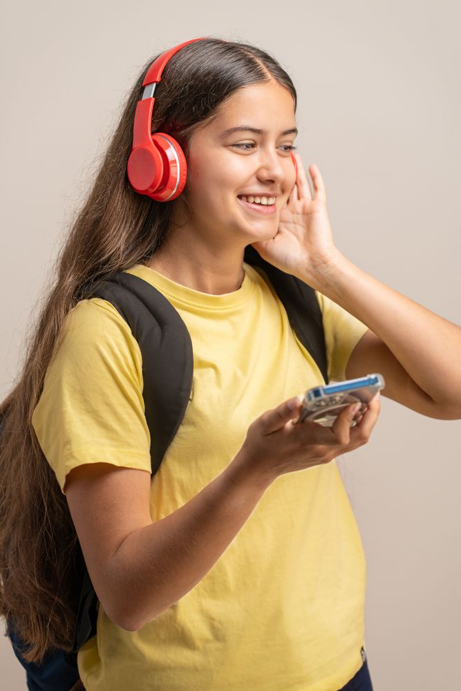 A happy young student smiling while listening to music on red headphones.