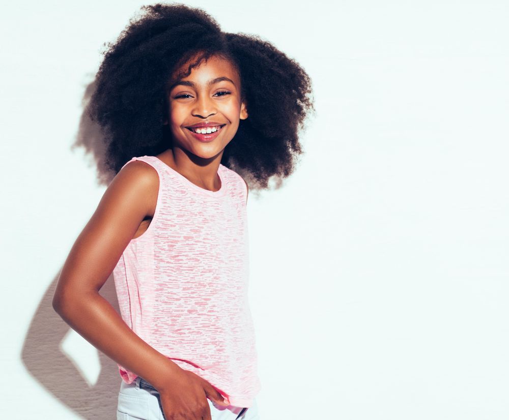 Studio portrait of young girl smiling in pink vest with hands in pocket