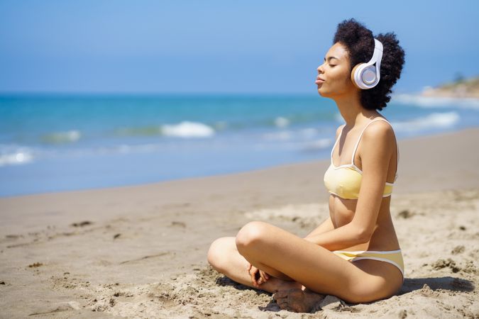 Woman in yellow swimwear sitting and meditating on beach