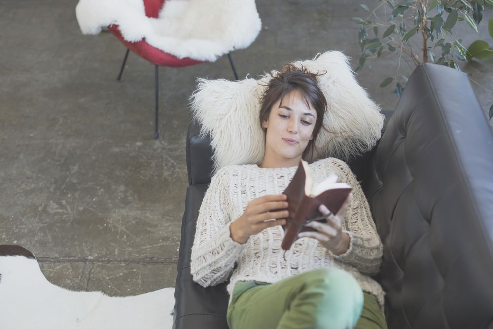 Looking down at female lying back with book on leather sofa