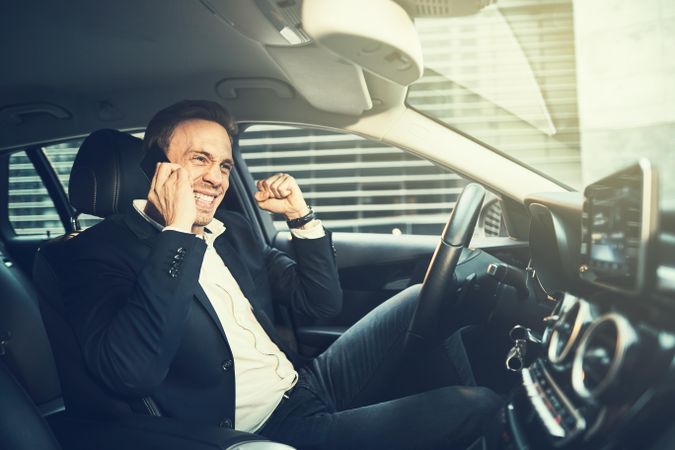 Happy man making a celebratory fist while talking on his cell phone in a vehicle