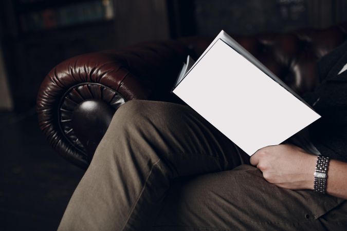 Side view of man sitting on brown couch reading a book