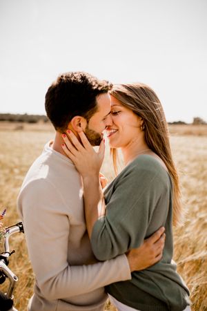 Sincere lovers posing by bicycle on rye field