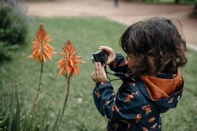 Little girl taking photos of orange flowers with small digital camera