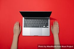 Top view of person’s hands resting next to laptop keyboard on red table 5pJvvb