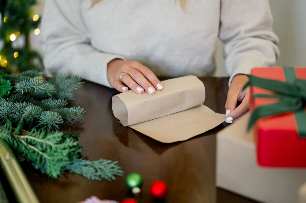 An unrecognizable woman is wrapping a Christmas gift in craft paper and a fir branch