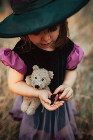 Young girl in witch hat looking down at her hand full of berries