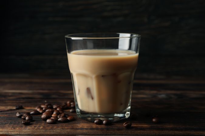 Glass of ice coffee on wooden background. Coffee seeds