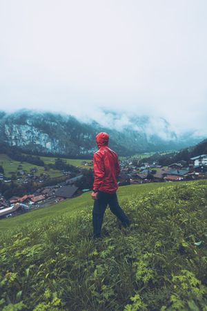 Man in red jacket walking on green grass field near village