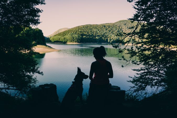 Woman with dog resting against beautiful lake