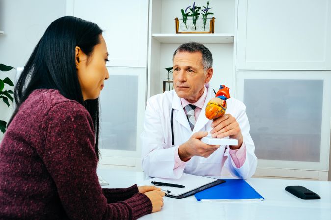 Concerned male doctor with serious female patient consulting about heart structure