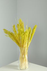 Vertical composition of vase with yellow reed grass in grey room
