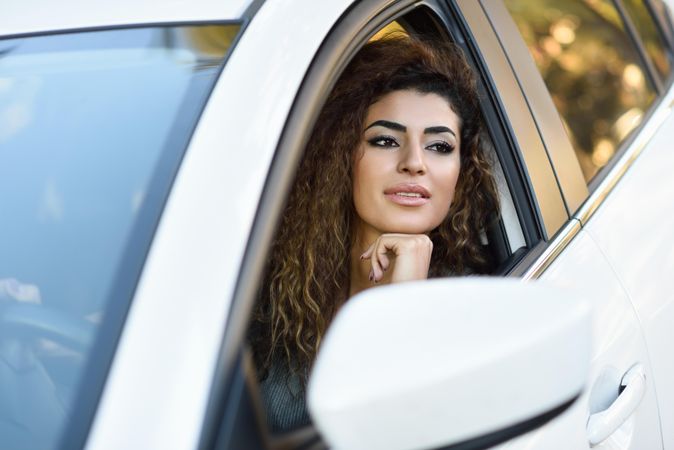 Smiling female with curly hair resting chin on hand out driver’s window
