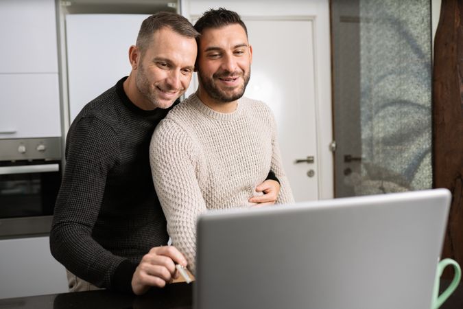 Male couple looking at laptop screen together in kitchen