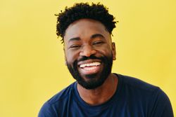 Portrait of joyful Black man in navy t-shirt in yellow studio