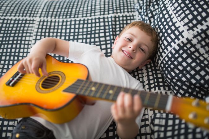 Young blonde boy playing toy guitar