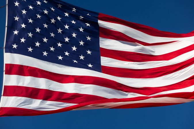 American Flag Waving In The Wind Against Deep Blue Sky.
