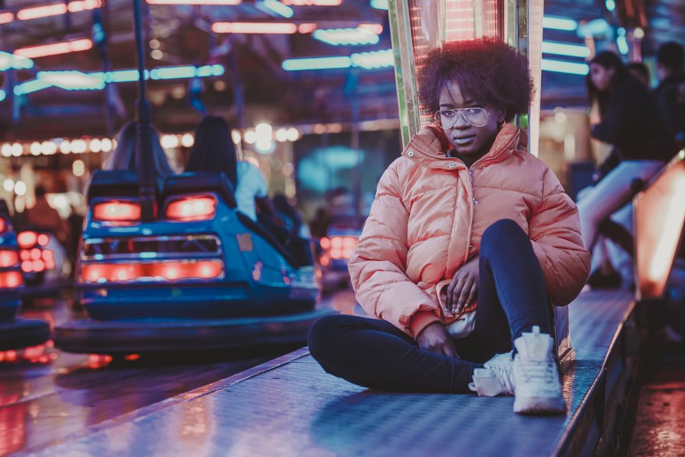 Black female sitting near attraction in amusement park