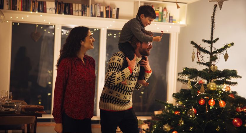 Man with his son on his shoulders helping him to decorate the Christmas tree