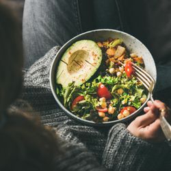 Woman in jeans and sweater eating bowl of fresh salad, top view, square crop