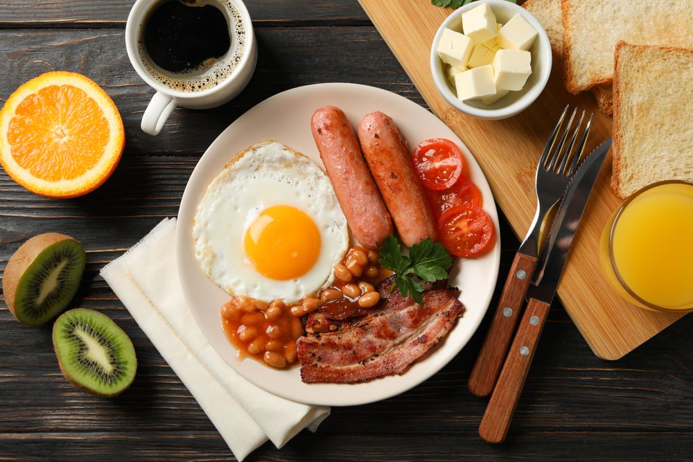 Top view of fried breakfast with kiwi, coffee and juice on table