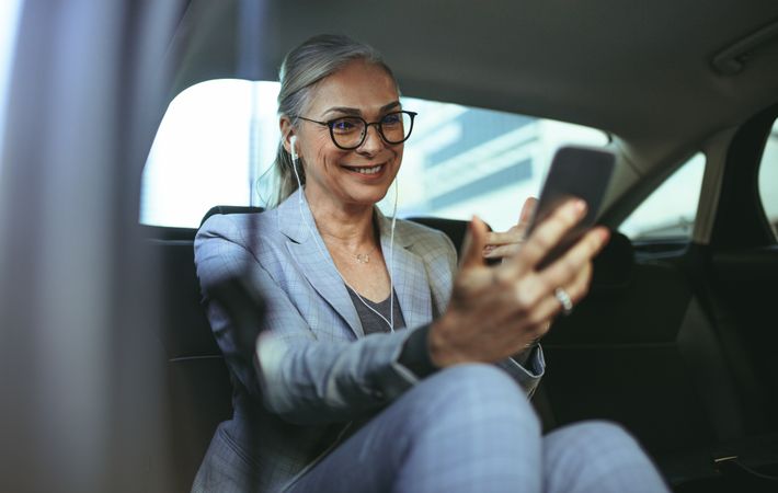 Female entrepreneur doing a video call with mobile phone while sitting on backseat of a car