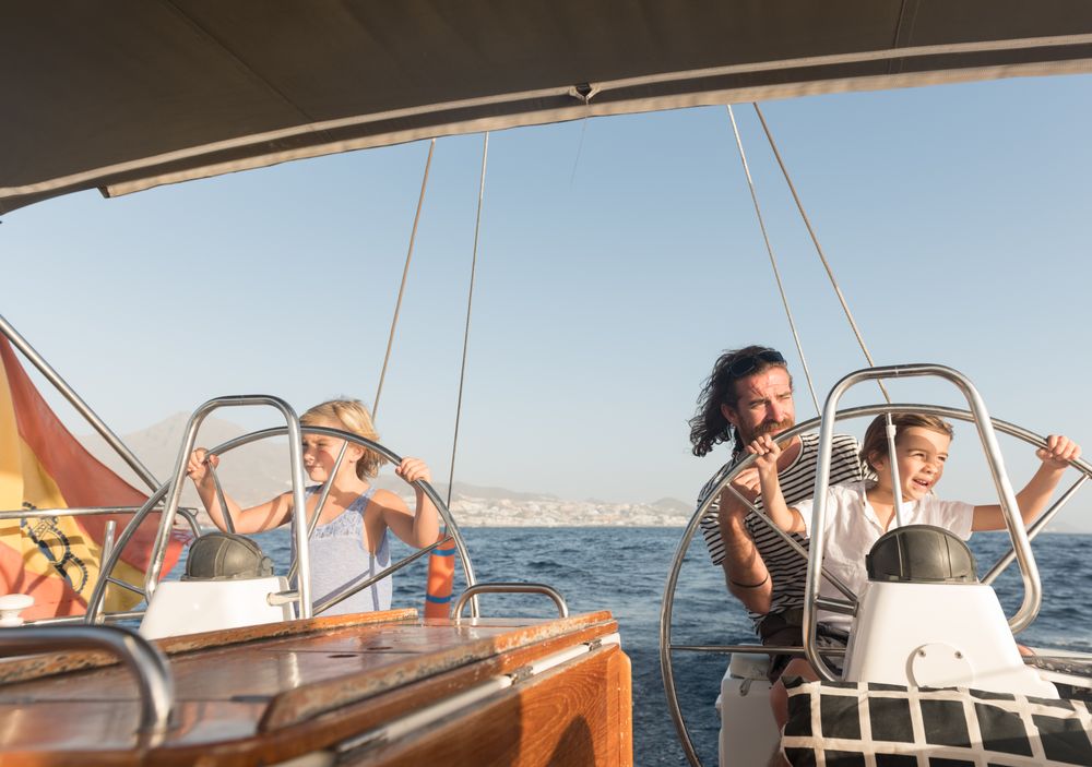 Man with boy and girl holding steering wheel on yacht on water